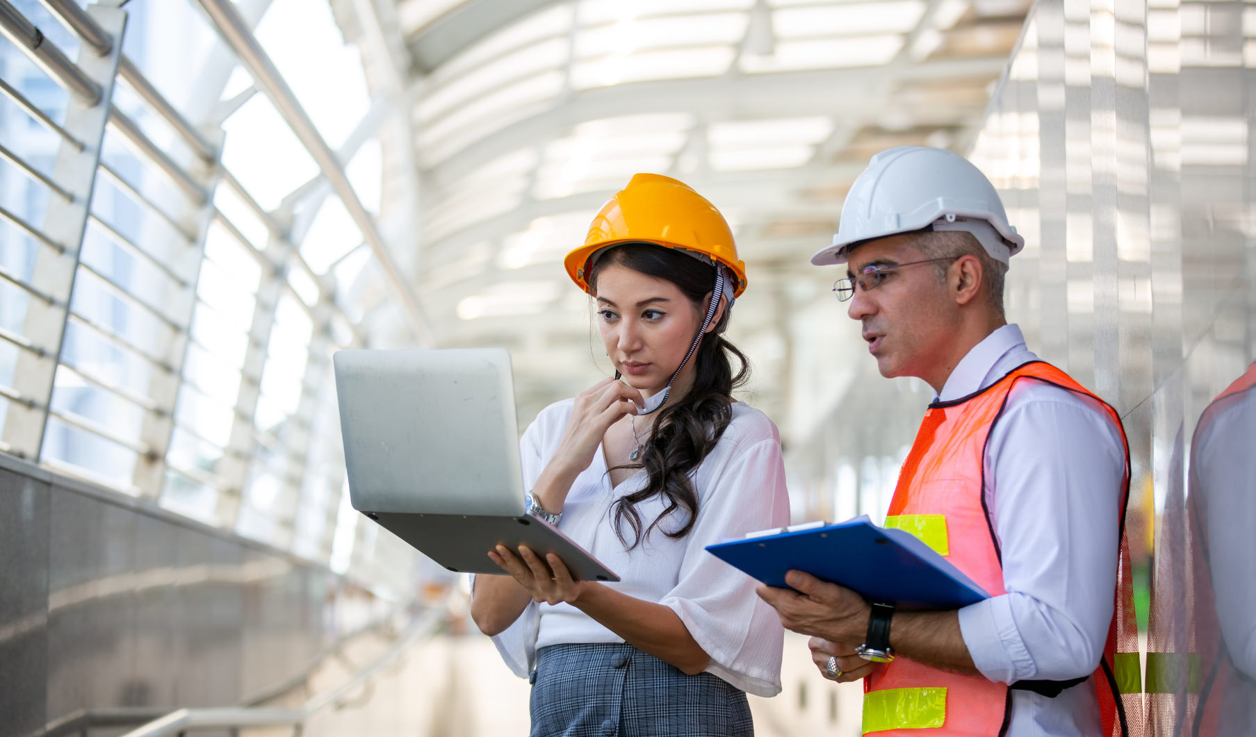 2 personas mirando hacia un portátil con vestimenta de prevención de riesgos laborales